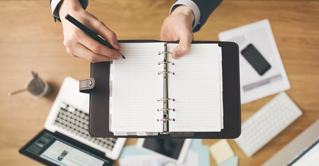 hands holding a pen and planner over a desk